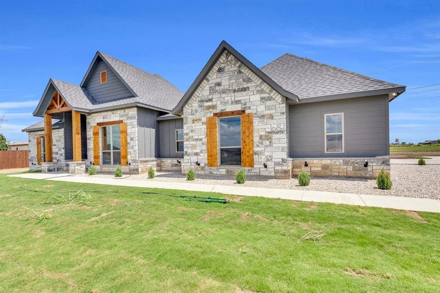 View of front of house with stone siding, roof with shingles, and a front lawn