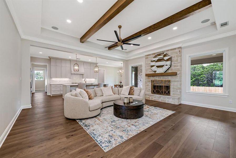 Living room with a stone fireplace, dark wood-type flooring, ceiling fan, beamed ceiling, and ornamental molding Living room with a stone fireplace, dark wood-type flooring, ceiling fan, beamed ceiling, and ornamental molding