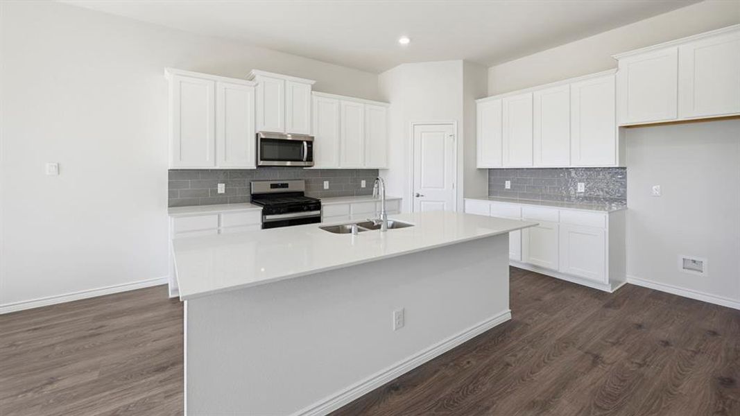 Kitchen featuring a large central island, white cabinetry, stainless steel appliances, grey subway tile backsplash, and wood-finish flooring