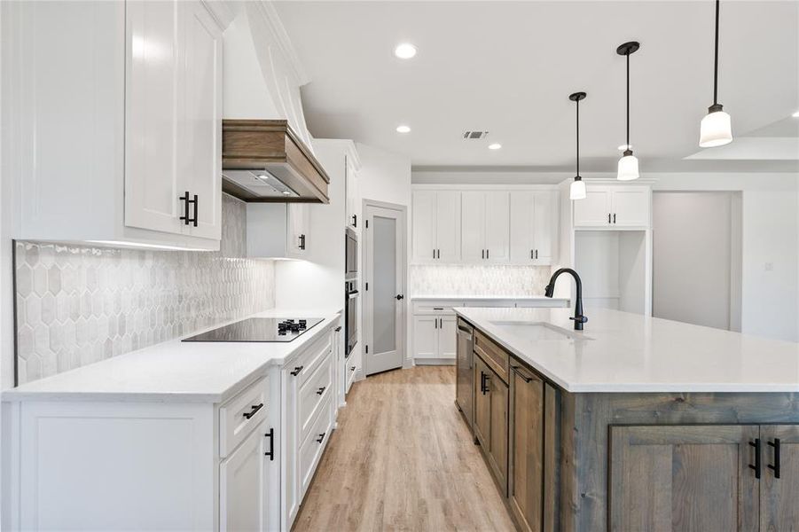 Kitchen with white cabinetry, backsplash, a kitchen island with sink, hanging light fixtures, and light wood-type flooring