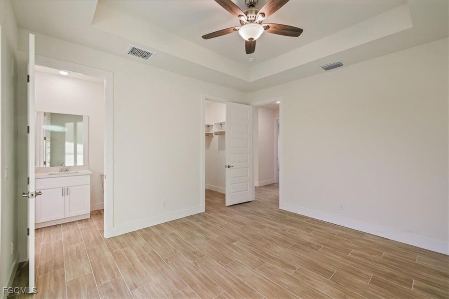 Unfurnished bedroom with a tray ceiling, a spacious closet, wood finish floors, a ceiling fan, and connected bathroom