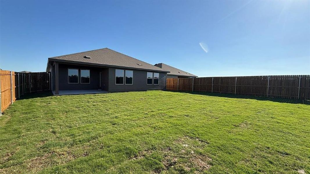 Spacious backyard with a large lawn, full privacy fencing, and a concrete patio