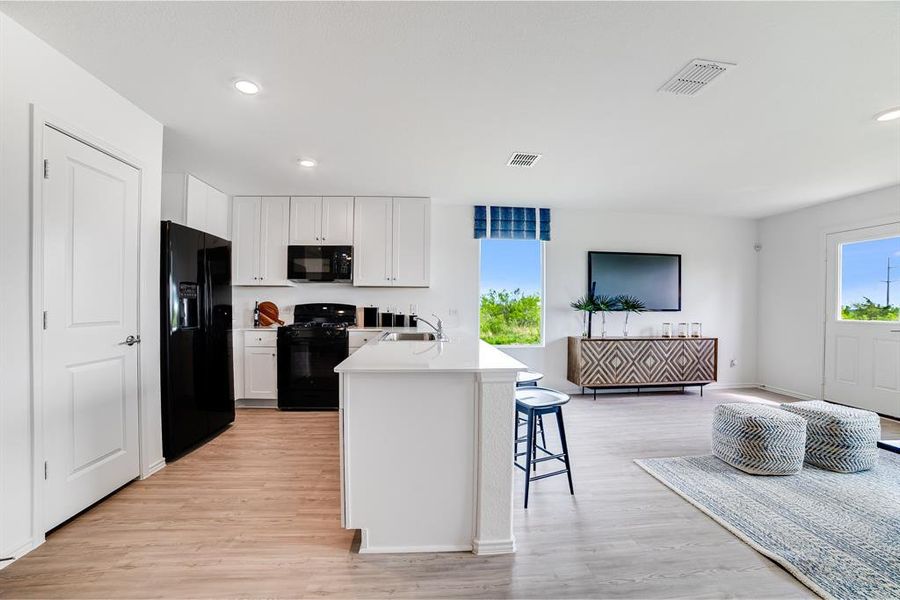 Kitchen with black appliances, light wood-type flooring, white cabinets, a kitchen bar, and recessed lighting Kitchen with black appliances, light wood-type flooring, white cabinets, a kitchen bar, and recessed lighting