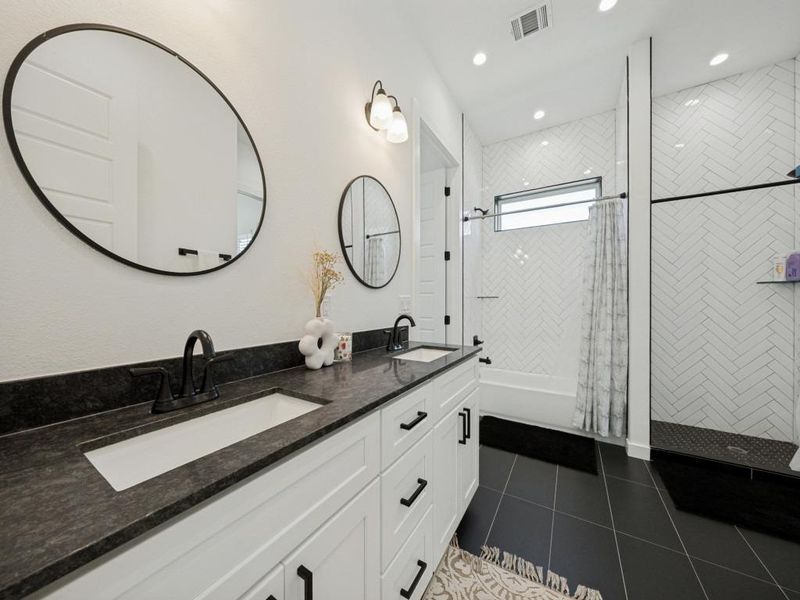 Dual vanities with sleek black countertops complement the modern shower with a white herringbone tile design. Dual vanities with sleek black countertops complement the modern shower with a white herringbone tile design.