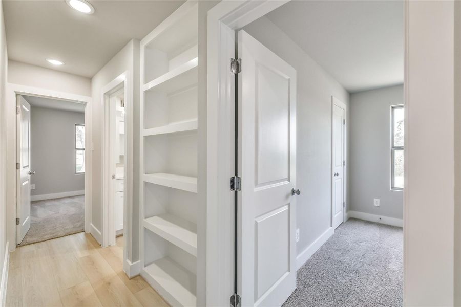 Hallway leading to the secondary bedrooms includes built-in shelving for extra storage and display, with both rooms offering natural light and cozy comfort.