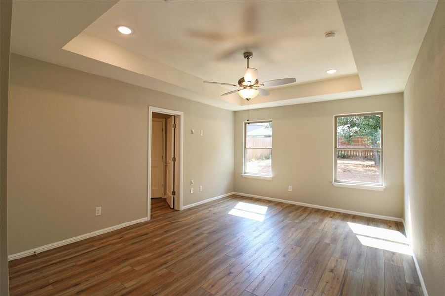 Spare room with a tray ceiling, wood finished floors, a ceiling fan, and recessed lighting
