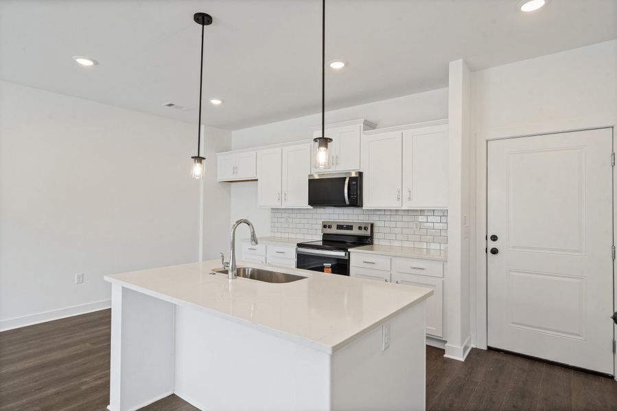 Kitchen featuring an island with a stainless steel sink, white cabinetry, subway tile backsplash, and stainless steel appliances Kitchen featuring an island with a stainless steel sink, white cabinetry, subway tile backsplash, and stainless steel appliances