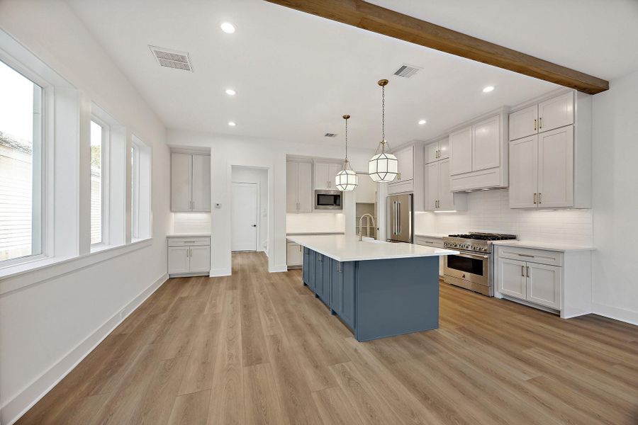 Well-appointed kitchen with modern flair featuring stainless steel appliances and a framed vent hood. The oversized bar overhang provides seating space for stools, while the walk-in pantry with a space-saving pocket door adds functionality. This chef’s kitchen is complete with soft-close drawers and cabinets designed for a smooth, silent finish