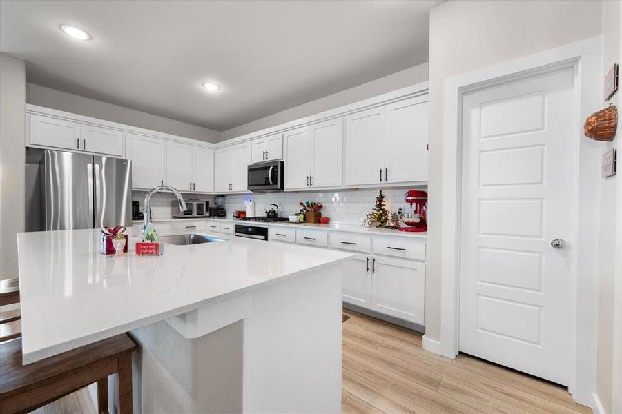 Kitchen with appliances with stainless steel finishes, white cabinets, a breakfast bar area, light stone counters, and a kitchen island with sink Kitchen with appliances with stainless steel finishes, white cabinets, a breakfast bar area, light stone counters, and a kitchen island with sink