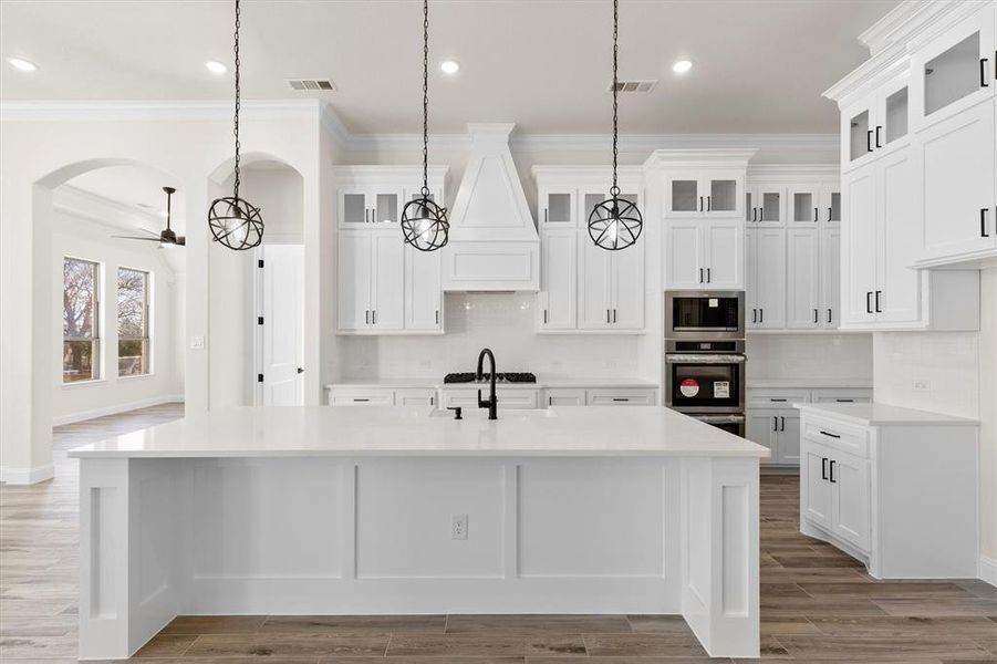 Kitchen featuring ornamental molding, decorative light fixtures, a center island with sink, and appliances with stainless steel finishes