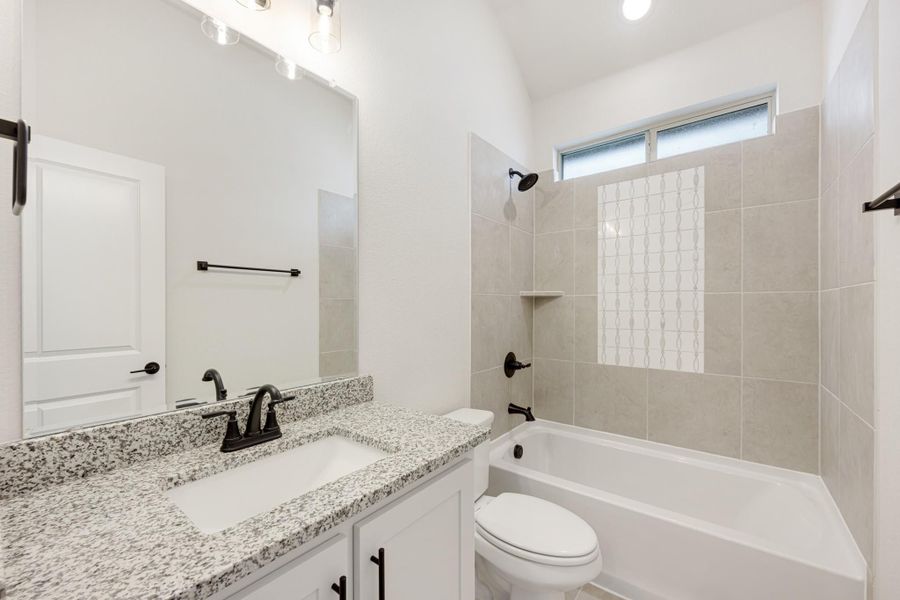 Bathroom with granite vanity, white cabinets, tub-shower combo with beige tile, and vaulted ceiling Bathroom with granite vanity, white cabinets, tub-shower combo with beige tile, and vaulted ceiling