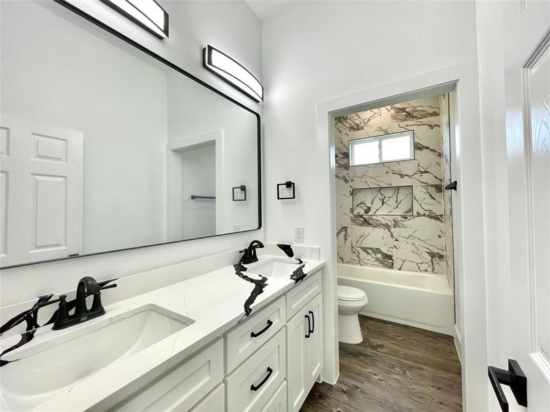 Full bath featuring bathing tub / shower combination, a sink, double vanity, toilet, and wood finished floors Full bath featuring bathing tub / shower combination, a sink, double vanity, toilet, and wood finished floors