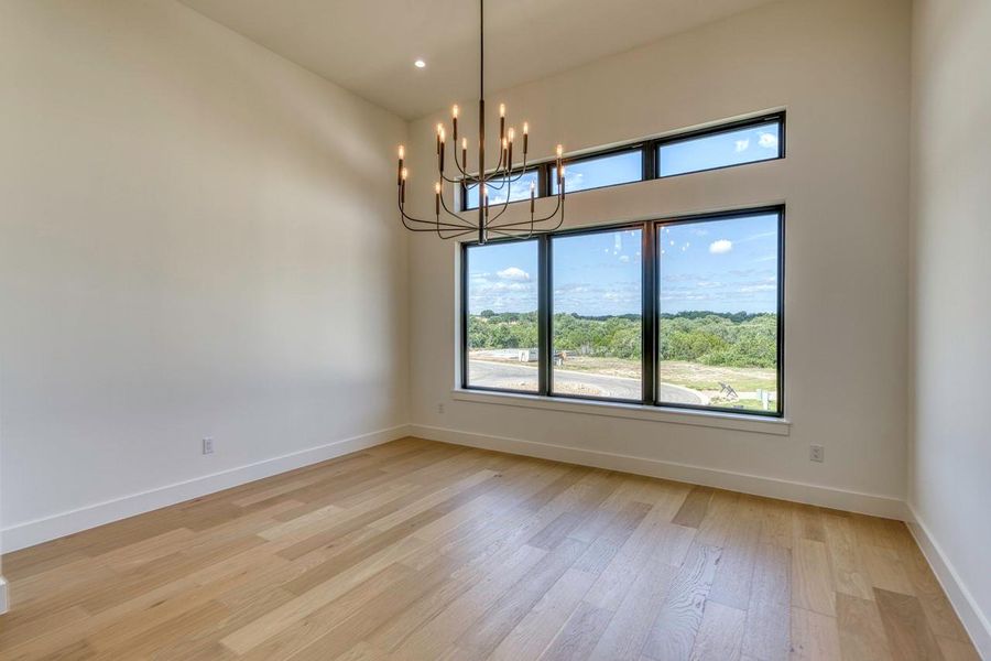 Large windows showcase peaceful green views from this airy room with elegant wood flooring.