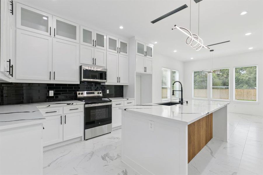 Kitchen with glass insert cabinets, appliances with stainless steel finishes, decorative backsplash, light stone countertops, and white cabinets