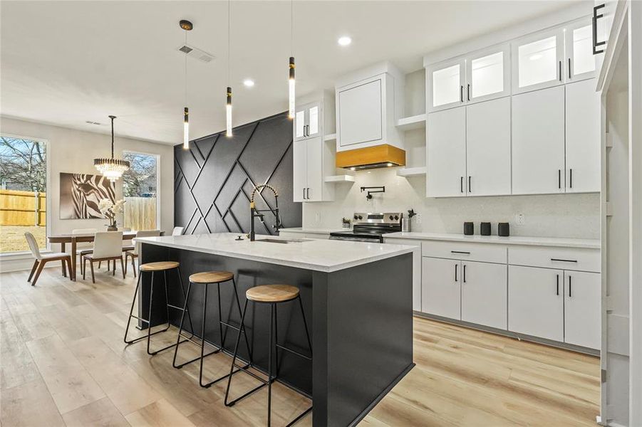 Dual tone kitchen featuring hanging light fixtures, a breakfast bar, light wood-style flooring, electric stove, and dual tone cabinets