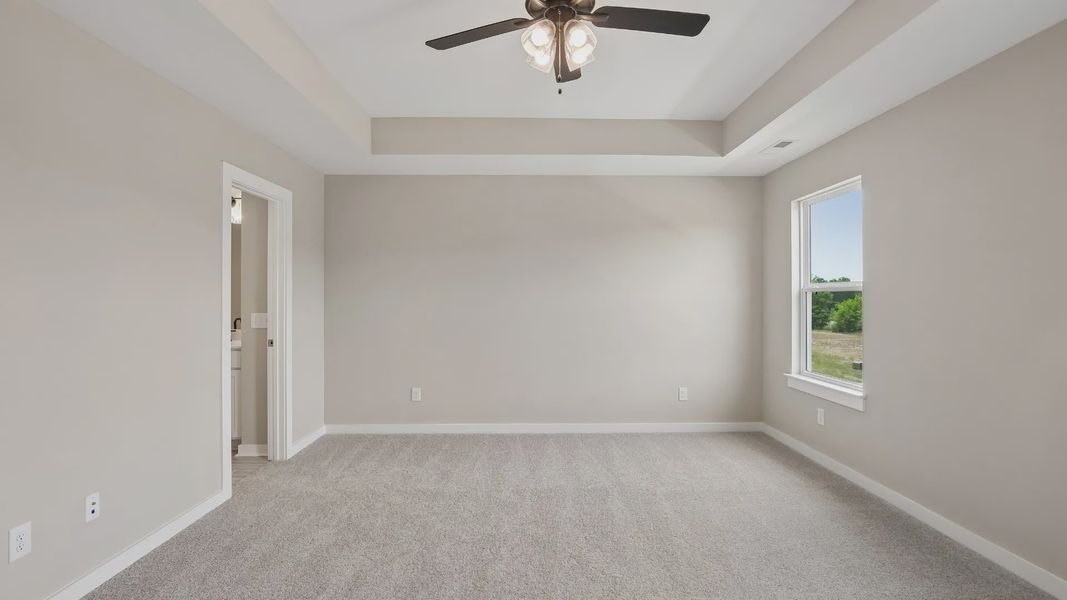 Bedroom with tray ceiling, windows, and en-suite primary bathroom Bedroom with tray ceiling, windows, and en-suite primary bathroom