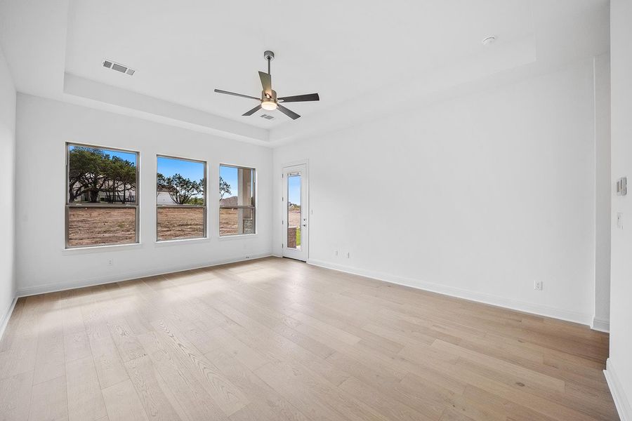 Unfurnished room featuring a tray ceiling, light wood-type flooring, and ceiling fan