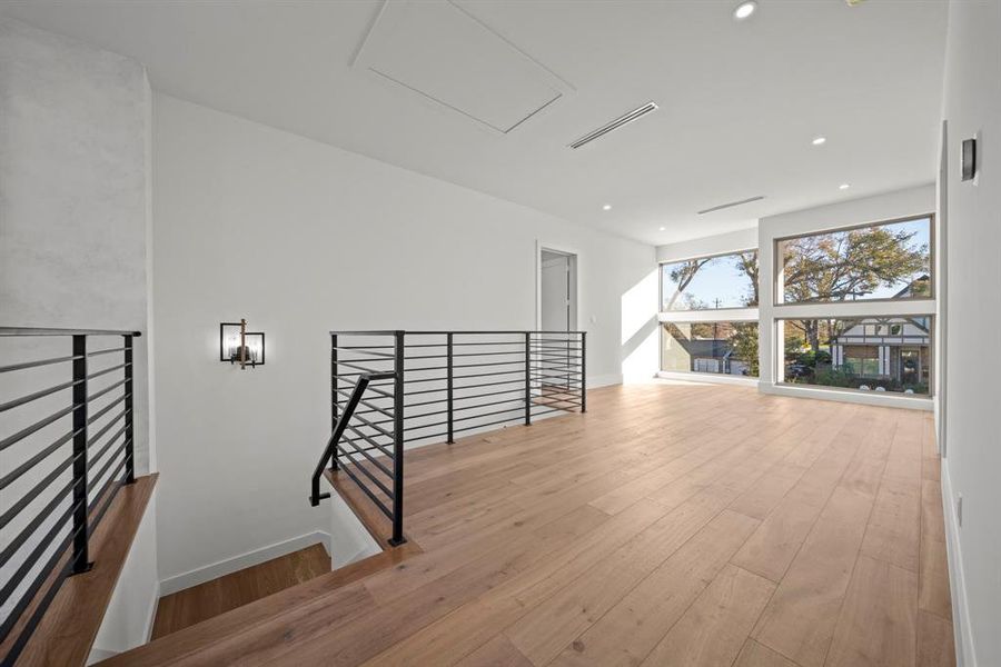 This expansive second-floor living area is filled with natural light, thanks to the oversized windows that offer beautiful neighborhood views. The sleek black railing adds a modern touch, while the warm wood flooring creates a cozy and inviting ambiance. Perfect for a family room, play area, or additional entertaining space, this versatile area combines functionality with contemporary design.