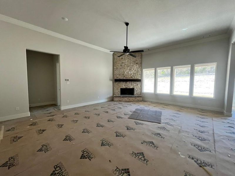 Unfurnished living room with a stone fireplace, ceiling fan, and ornamental molding