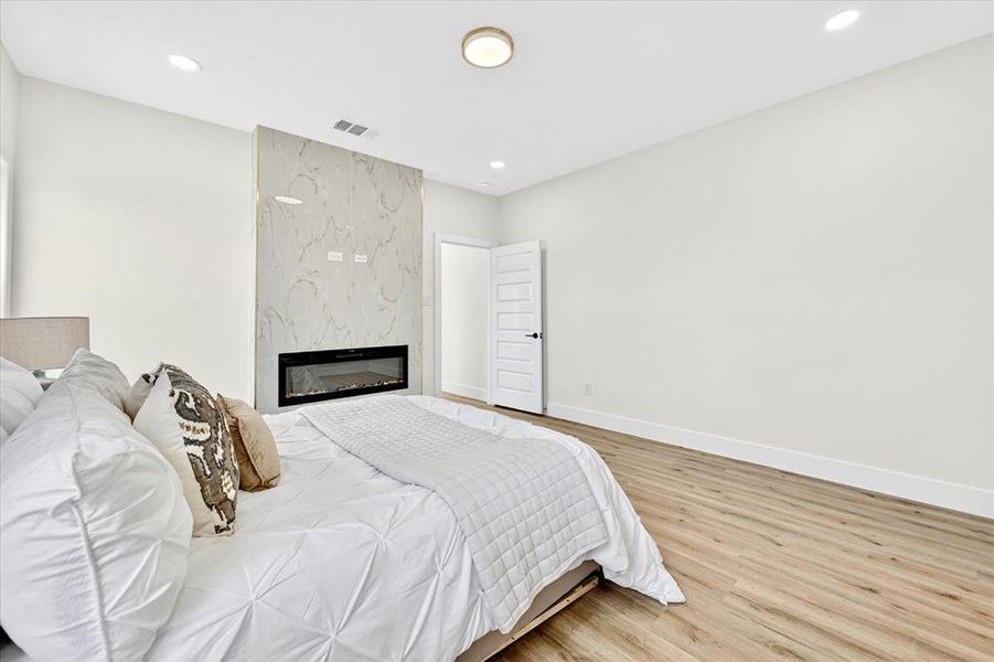 Spacious room featuring a contemporary accent wall with a built-in fireplace, wood-finish flooring, recessed lighting, and a solid core door