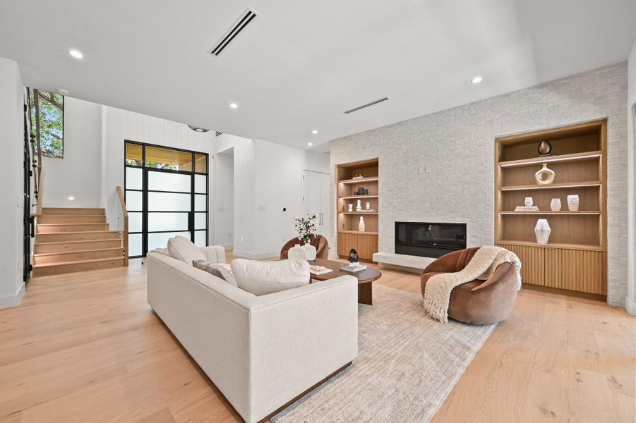 Living area with built in shelves, stairs, recessed lighting, a large fireplace, and light wood-style floors