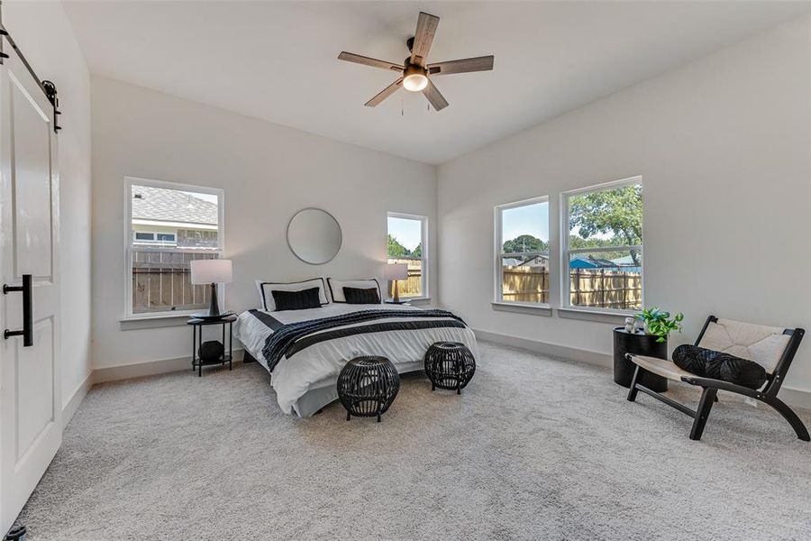 Carpeted primary bedroom featuring a barn door and ceiling fan