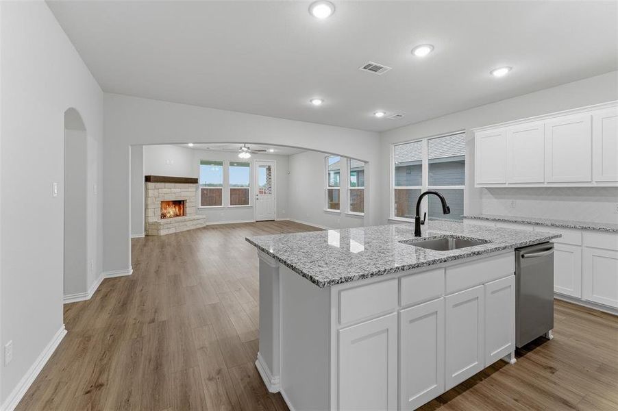 Kitchen island featuring a stainless steel sink with a matte black faucet, granite countertops, white cabinetry, and wood-finish flooring Kitchen island featuring a stainless steel sink with a matte black faucet, granite countertops, white cabinetry, and wood-finish flooring