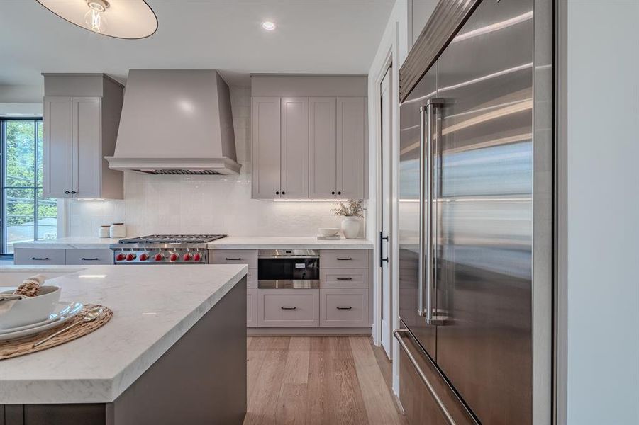 Kitchen featuring appliances with stainless steel finishes, wall chimney range hood, tasteful backsplash, light wood-style floors, and light stone countertops