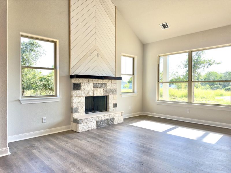 Unfurnished living room with healthy amount of natural light, dark wood-style flooring, a fireplace, and high vaulted ceiling Unfurnished living room with healthy amount of natural light, dark wood-style flooring, a fireplace, and high vaulted ceiling