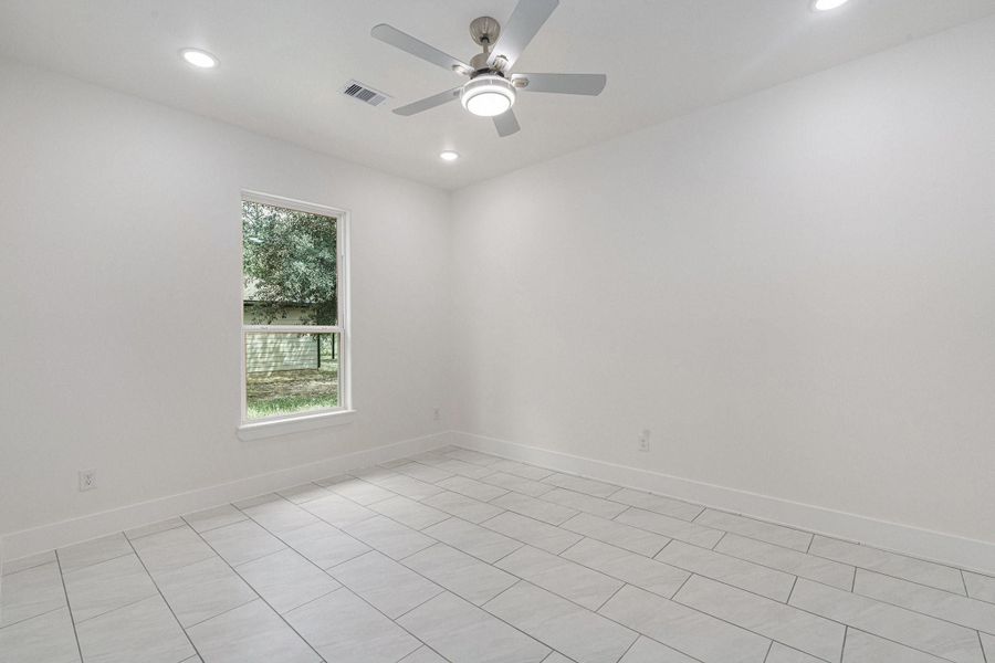 Bright, spacious room with white walls and tiled flooring. It features a ceiling fan and recessed lighting, with a window providing natural light and a view of greenery outside. Bright, spacious room with white walls and tiled flooring. It features a ceiling fan and recessed lighting, with a window providing natural light and a view of greenery outside.