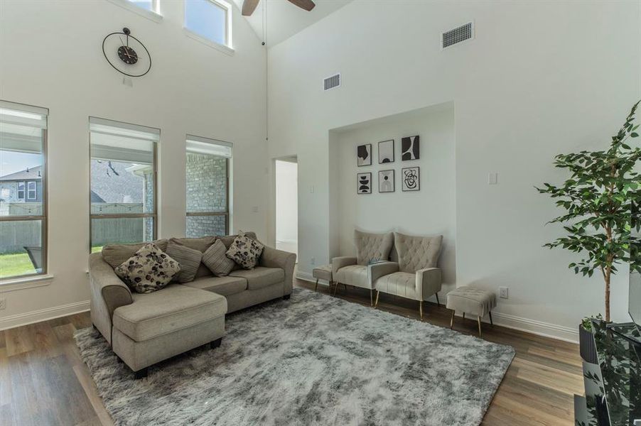 Spacious living area featuring high ceilings, upper transom windows, multiple large windows, wood-finish flooring, and recessed wall alcove
