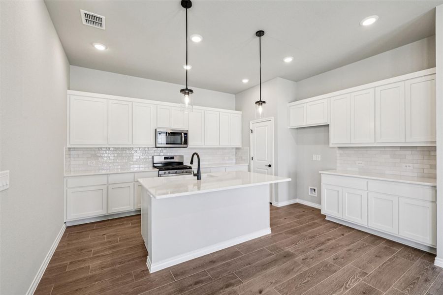 Kitchen featuring appliances with stainless steel finishes, backsplash, dark wood-style floors, white cabinets, and a kitchen island with sink Kitchen featuring appliances with stainless steel finishes, backsplash, dark wood-style floors, white cabinets, and a kitchen island with sink