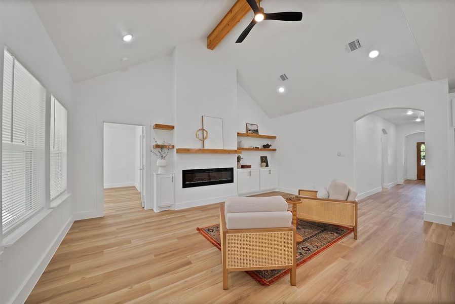 Living room featuring beamed ceiling, arched walkways, light wood finished floors, high vaulted ceiling, and a glass covered fireplace