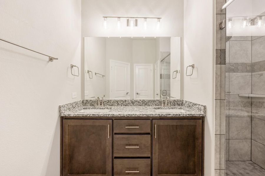 Bathroom with double sink vanity, granite countertop, dark wood cabinets, and tiled walk-in shower
