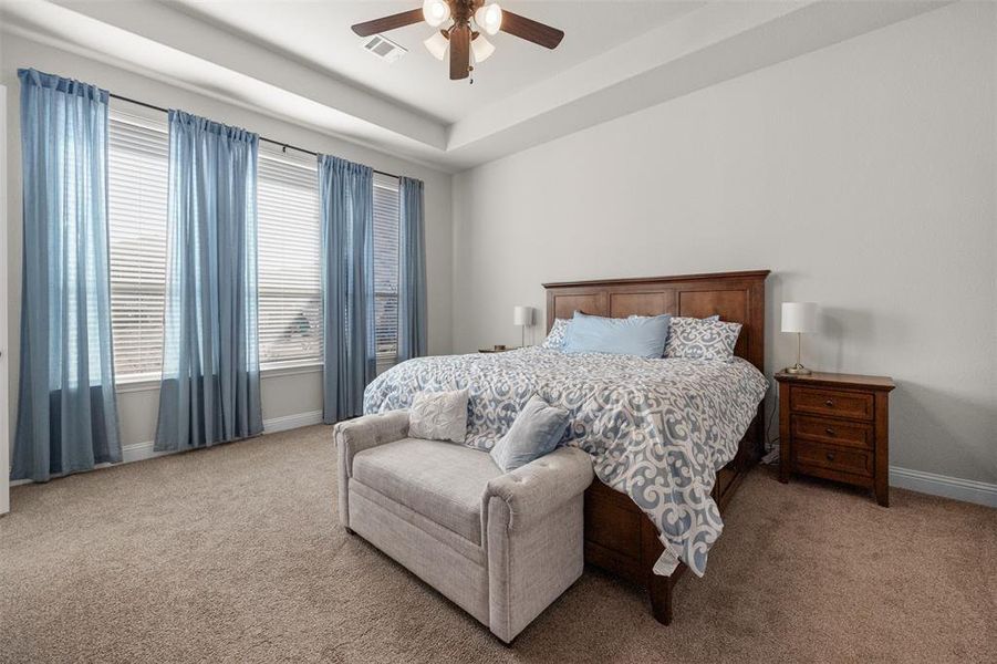 Bedroom featuring light carpet, a tray ceiling, and ceiling fan Bedroom featuring light carpet, a tray ceiling, and ceiling fan