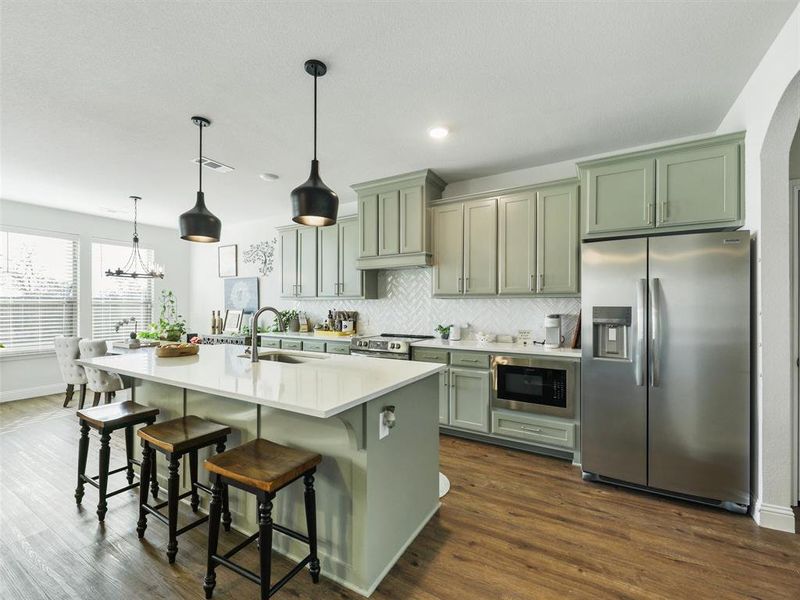 Kitchen with a kitchen bar, appliances with stainless steel finishes, a kitchen island with sink, pendant lighting, and sink