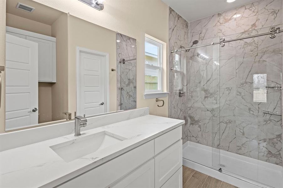 Full bathroom with vanity, a marble finish shower, and visible vents