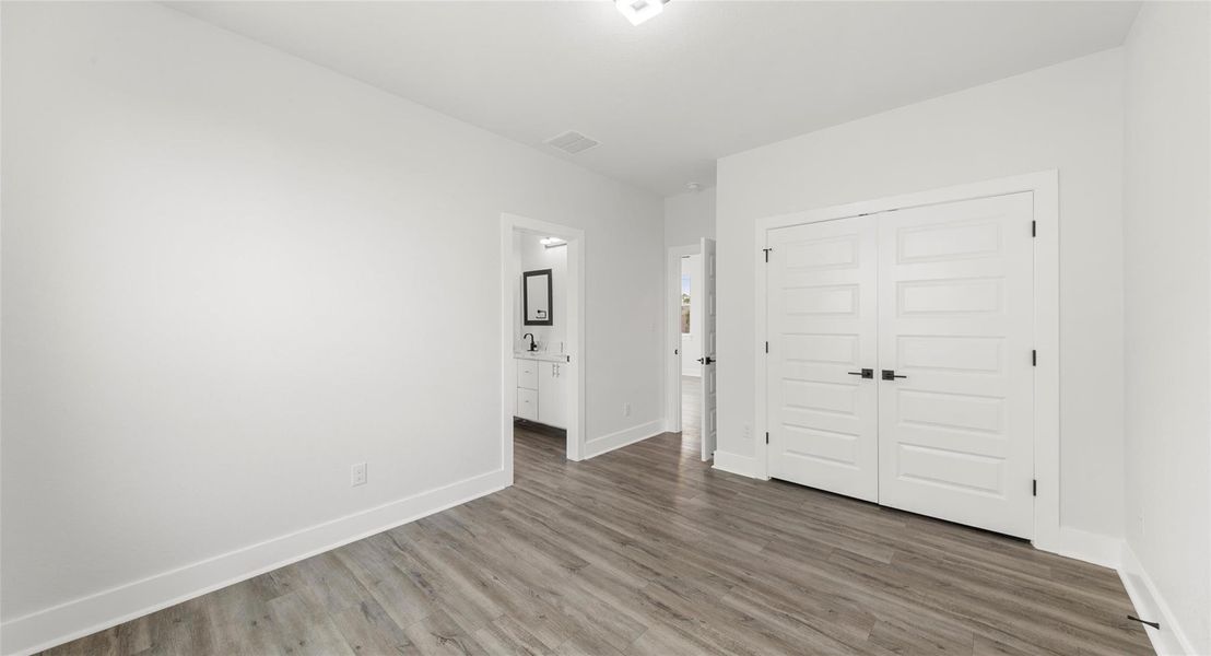 Unfurnished bedroom with wood finished floors, a closet, and connected bathroom