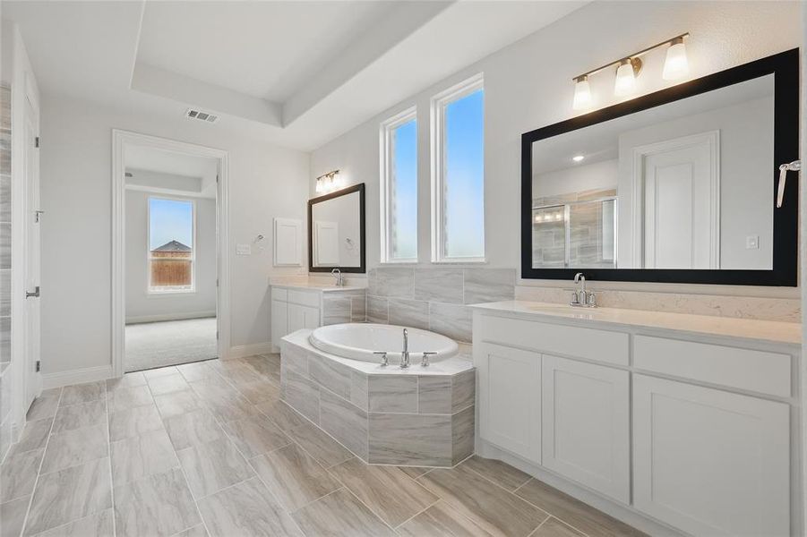 Bathroom with a sink, a stall shower, a garden tub, visible vents, and two vanities