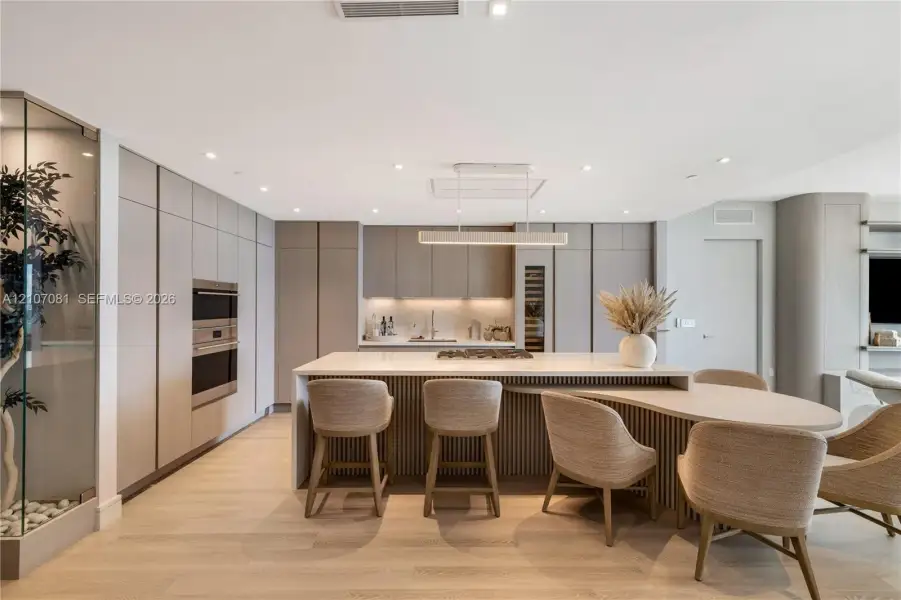 Modern kitchen featuring floor-to-ceiling cabinetry, a central island with integrated seating, built-in stainless steel appliances, wood-finish flooring, and recessed lighting Modern kitchen featuring floor-to-ceiling cabinetry, a central island with integrated seating, built-in stainless steel appliances, wood-finish flooring, and recessed lighting
