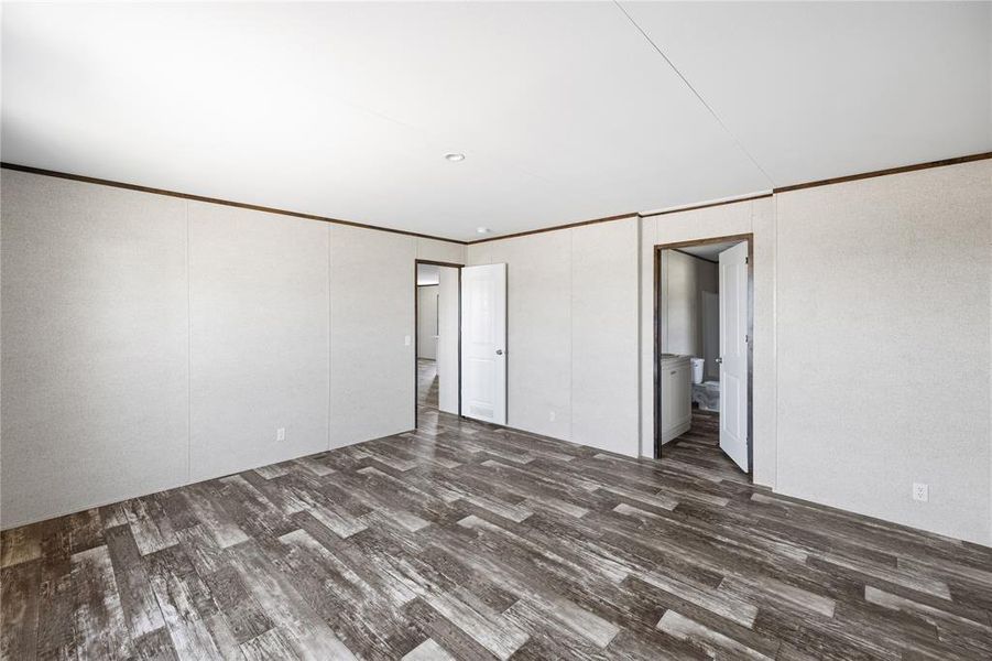 Unfurnished bedroom featuring ensuite bathroom, ornamental molding, and dark hardwood / wood-style flooring