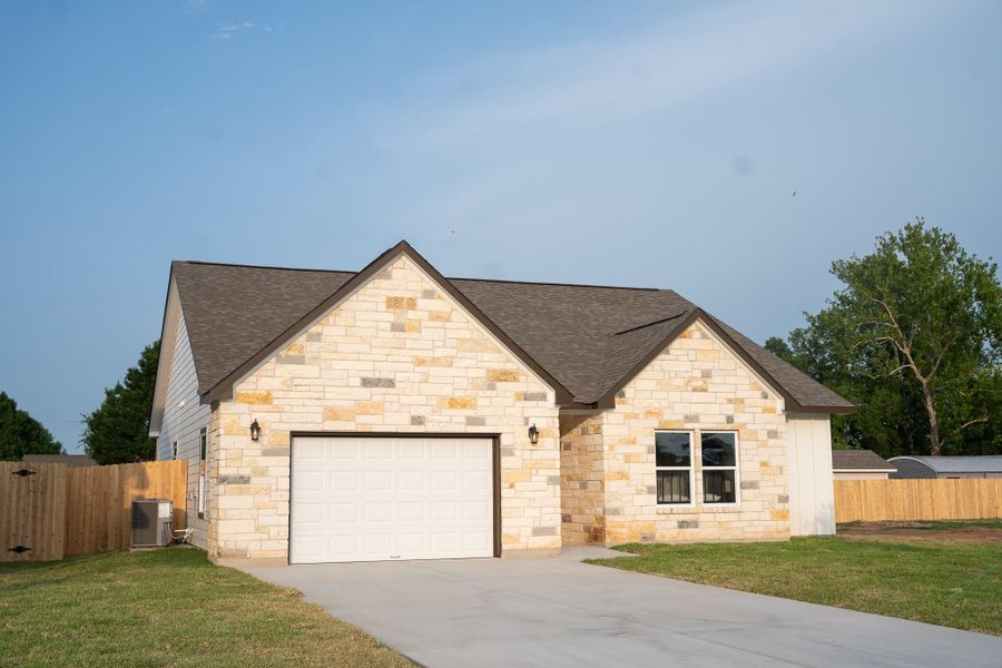 French country inspired facade with roof with shingles, a garage, concrete driveway, and stone siding