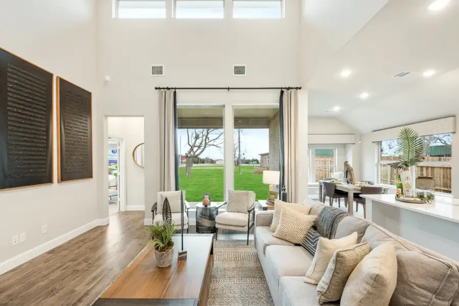 Open living room with high ceilings, hardwood floors, and large sliding glass doors overlooking a green backyard