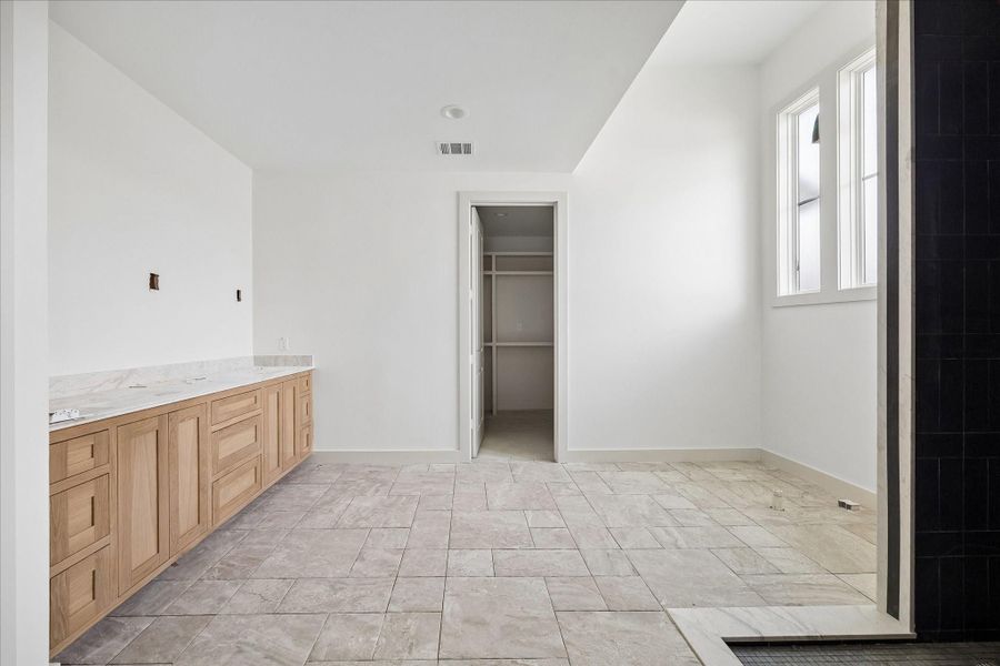 Spa inspired primary bathroom featuring an expansive double vanity with warm wood cabinetry and sleek quartz countertops, offering both style and functionality. The oversized walk in shower plus freestanding soaking tub creates a clean, modern focal point, while the thoughtful layout provides ample space for daily routines. Natural light from well placed windows enhances the bright, serene atmosphere, and direct access to the spacious walk in closet adds convenience to this well designed retreat.
