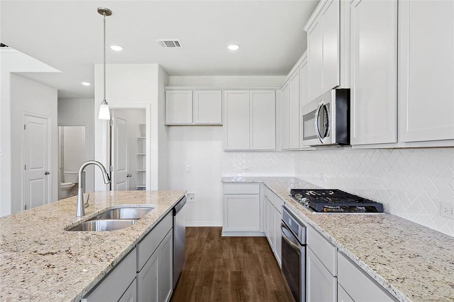 Kitchen featuring dark hardwood / wood-style floors, hanging light fixtures, tasteful backsplash, appliances with stainless steel finishes, and sink