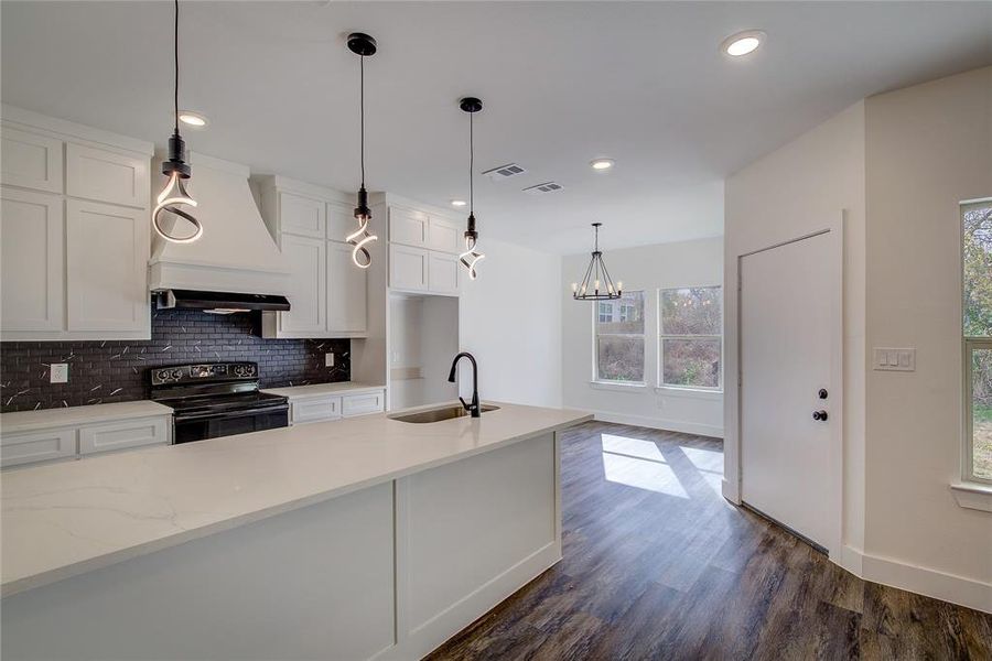 Kitchen with black range with electric stovetop, tasteful backsplash, white cabinetry, hanging light fixtures, and custom range hood Kitchen with black range with electric stovetop, tasteful backsplash, white cabinetry, hanging light fixtures, and custom range hood