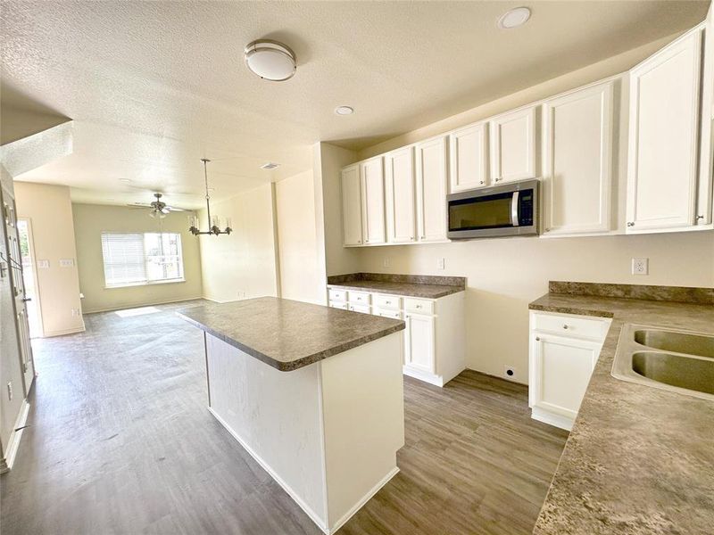 Kitchen featuring stainless steel microwave, white cabinets, a kitchen island, a textured ceiling, and light wood-style flooring
