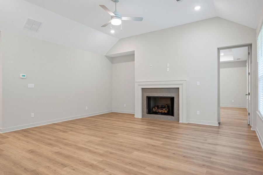 Vaulted ceilings featuring a ceiling fan and recessed lighting, wood-finish flooring, and a fireplace with a stone surround and a white mantel Vaulted ceilings featuring a ceiling fan and recessed lighting, wood-finish flooring, and a fireplace with a stone surround and a white mantel