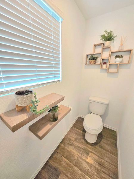 Powder room featuring wood-finish flooring, a white toilet, and a window with blinds