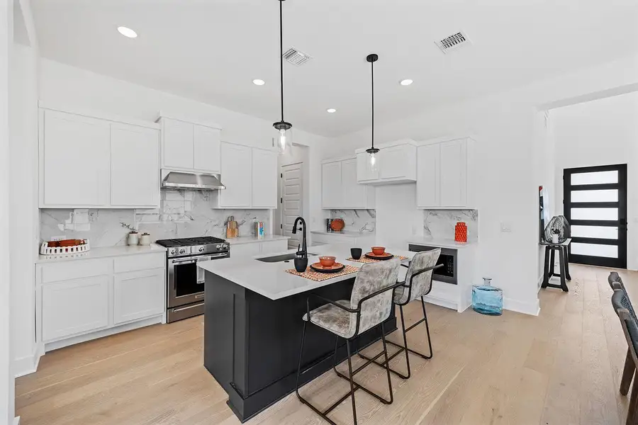 Kitchen featuring light wood-flooring, dark cabinets, white cabinetry, stainless steel gas stove, and recessed lighting